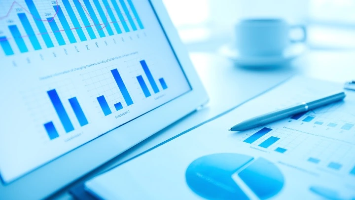 Sobre un escritorio limpio descansa un bolígrafo, unas hojas con datos contables y una pantalla. En la pantalla del ordenador se muestra un dashborad financiero.