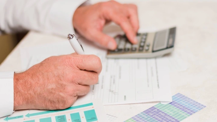 Unas manos de hombre trabajan con fcturas y con una calculadora.