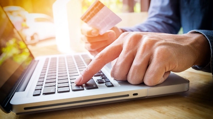 Persona utilizando un ordenador portátil mientras sostiene una tarjeta bancaria, realizando una operación financiera o pago online.