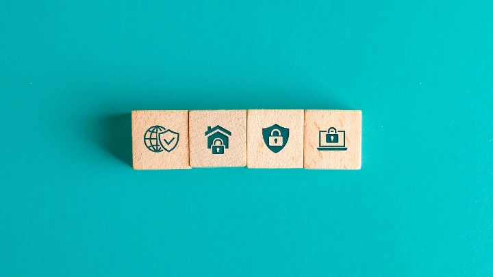 Cubos de madera con iconos de seguridad, vivienda y datos digitales, simbolizando la protección de datos y la seguridad de la información en entornos digitales.